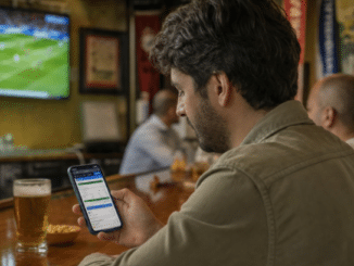 Hombre consulta en su móvil la app de una casa de apuestas mientras ve un partido de fútbol en un bar.